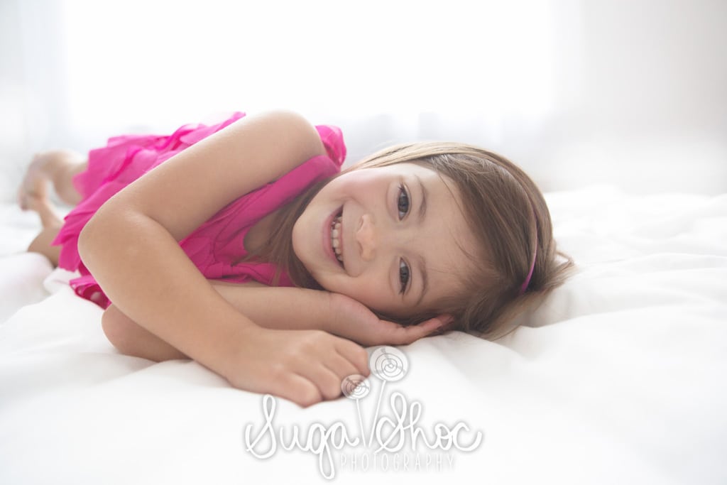 SugaShoc_Photography_Children_Photographer_Bucks County_Doylestown_PA_girl_posed_on_bed_pink_dress_smiling