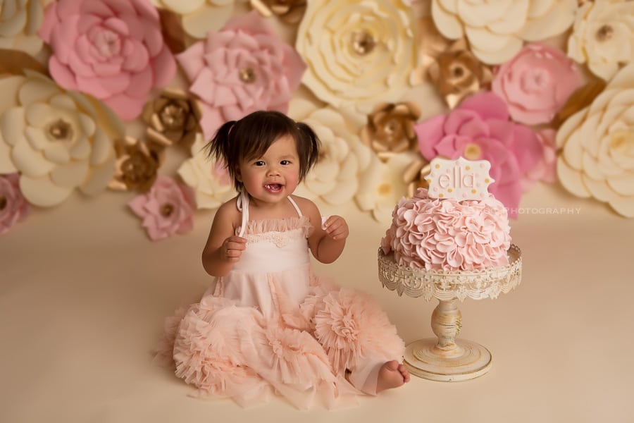 sugashoc_photography_cake_smash_photographer_bucks_county_pa_doylestown_pa_first_birthday_smash_cake_flowers_background_smiling_toddler