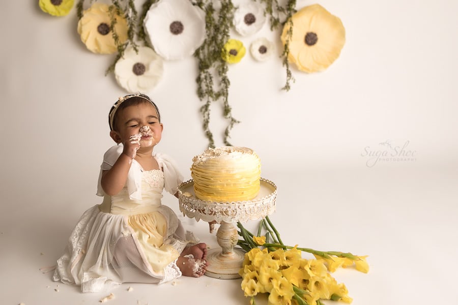SugaShoc_Photography_Cake_Smash_Photographer_Bucks_County_PA_Doylestown_PA_Cream_and_yellow_theme_frosting_on_nose_cake_on_feet_yellow_flowers