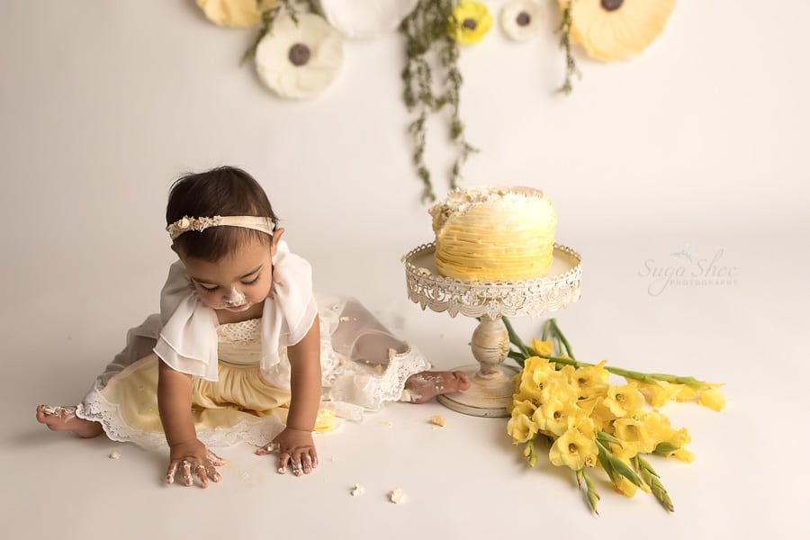 SugaShoc_Photography_Cake_Smash_Photographer_Bucks_County_PA_Doylestown_PA_Cream_and_yellow_theme_cake_on_floor_cake_on_hands_yellow_Flowers