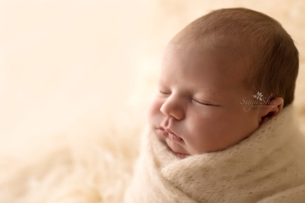 SugaShoc Photography Newborn Photographer Bucks County PA Doylestown PA Neutral Tones Baby sleeping wrapped up in cream knit wrap sitting on cream flokati