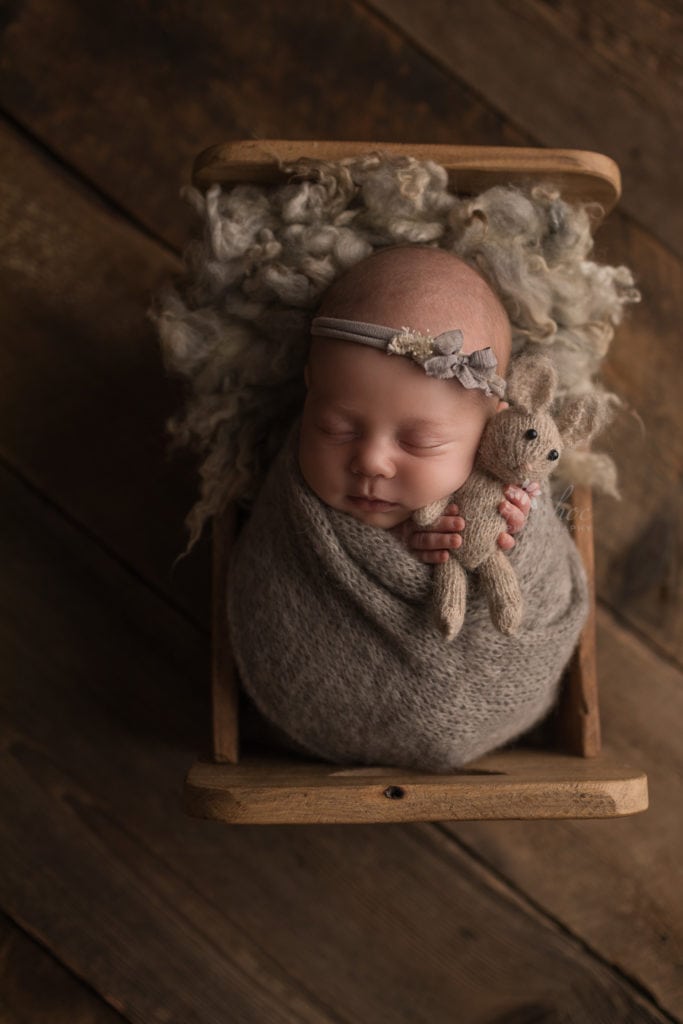 SugaShoc Photography Newborn Photographer Bucks County PA Doylestown PA Neutral Tones Baby girl wrapped in light brown with light brown headband sleeping in wooden bed with brown bear 