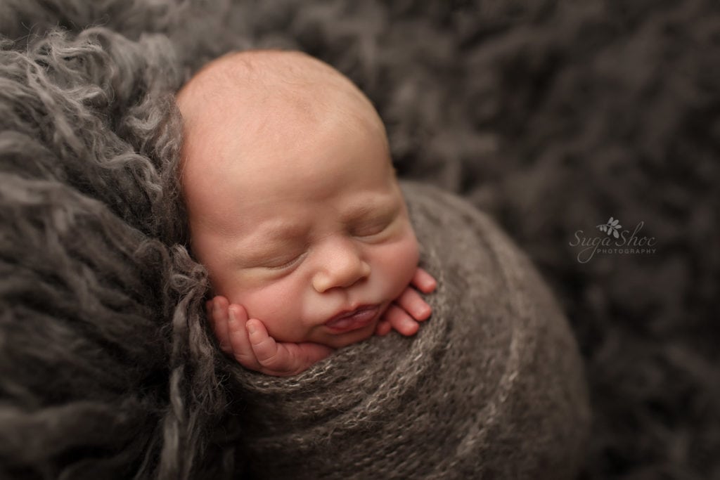 SugaShoc Photography Newborn Photographer Bucks County PA Doylestown PA Neutral Tones Baby boy wrapped in charcoal gray knit wrap with hands sticking out laying on gray flokati