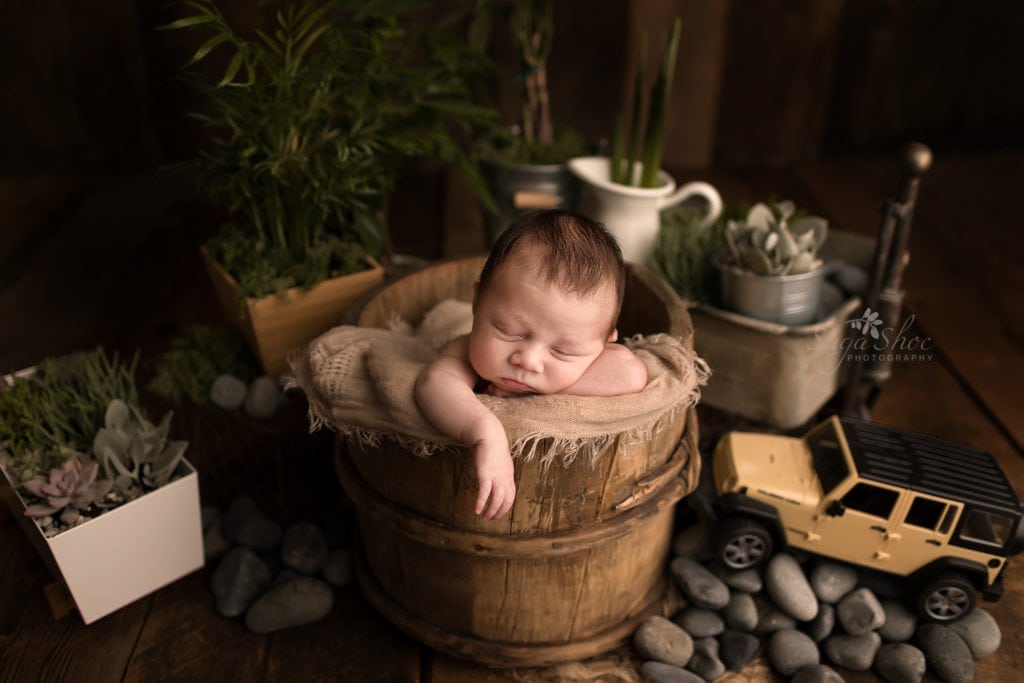 SugaShoc Photography Newborn Photographer Bucks County PA Doylestown PA Neutral Tones Baby boy sleeping in wooden bucket with beige blanket with various plants, rocks and natural elements around him