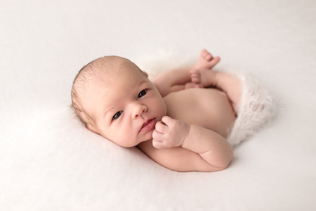 SugaShoc Photography Newborn Photographer Bucks County PA Doylestown PA Keeping Babies Asleep Baby boy awake laying on white blanket with legs wrapped in white knit
