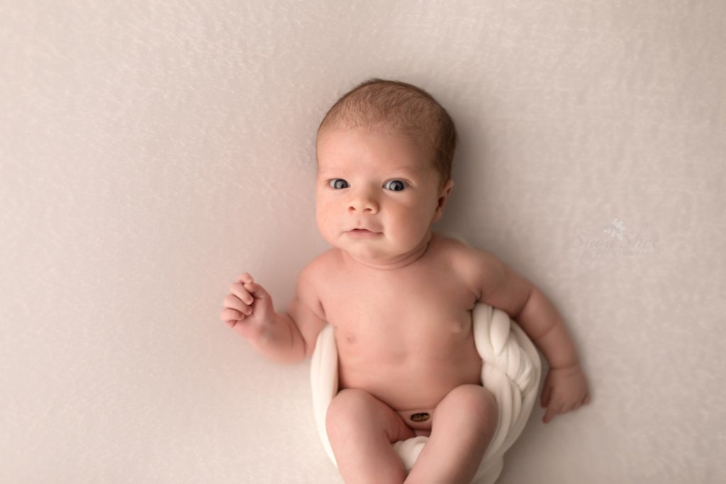 SugaShoc Photography Newborn Photographer Bucks County PA Doylestown PA Keeping Babies Asleep Baby boy awake laying white blanket with tushy in cream wrap looking at camera