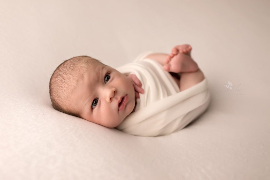 SugaShoc Photography Newborn Photographer Bucks County PA Doylestown PA Keeping Babies Asleep Baby boy awake wrapped in cream wrap with feet sticking out 