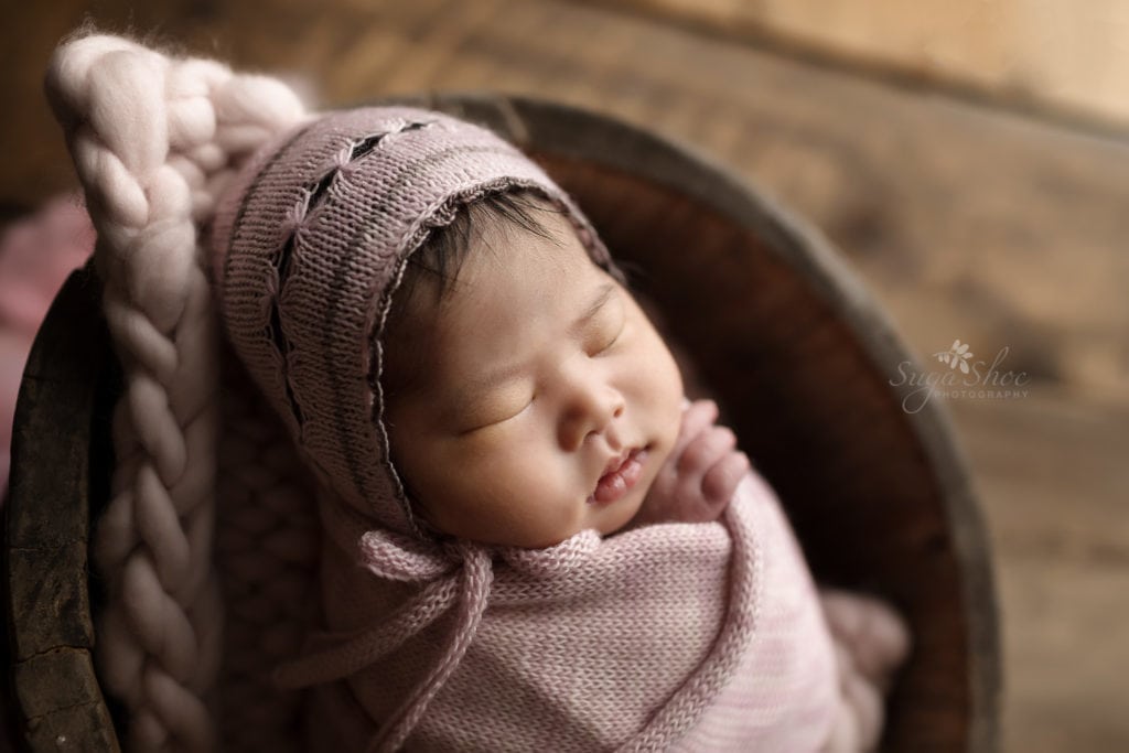 SugaShoc Photography Newborn Photographer Bucks County PA Doylestown PA Sophia's Newborn Session Baby girl sleeping wooden bucket wrapped in pale purple wrap and matching hat on a purple chunky knit blanket