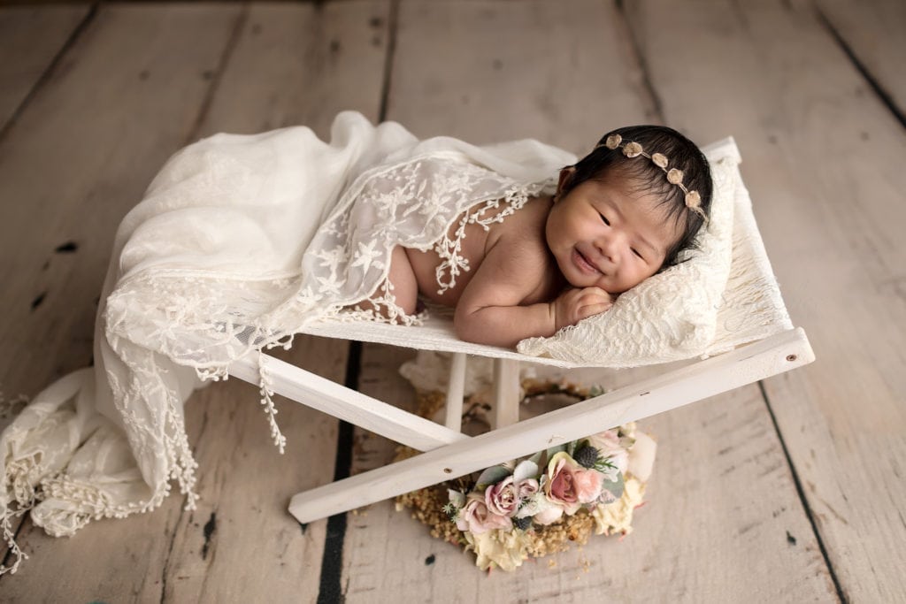 SugaShoc Photography Newborn Photographer Bucks County PA Doylestown PA Sophia's Newborn Session Baby girl awake laying on white sling bed with white throw and a floral headband