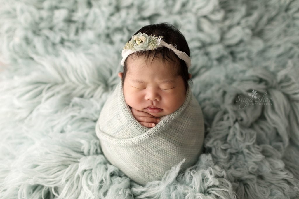 SugaShoc Photography Newborn Photographer Bucks County PA Doylestown PA Sophia's Newborn Session Baby girl sleeping wrapped in pale blue wearing a floral headband on a pale blue flokati rug