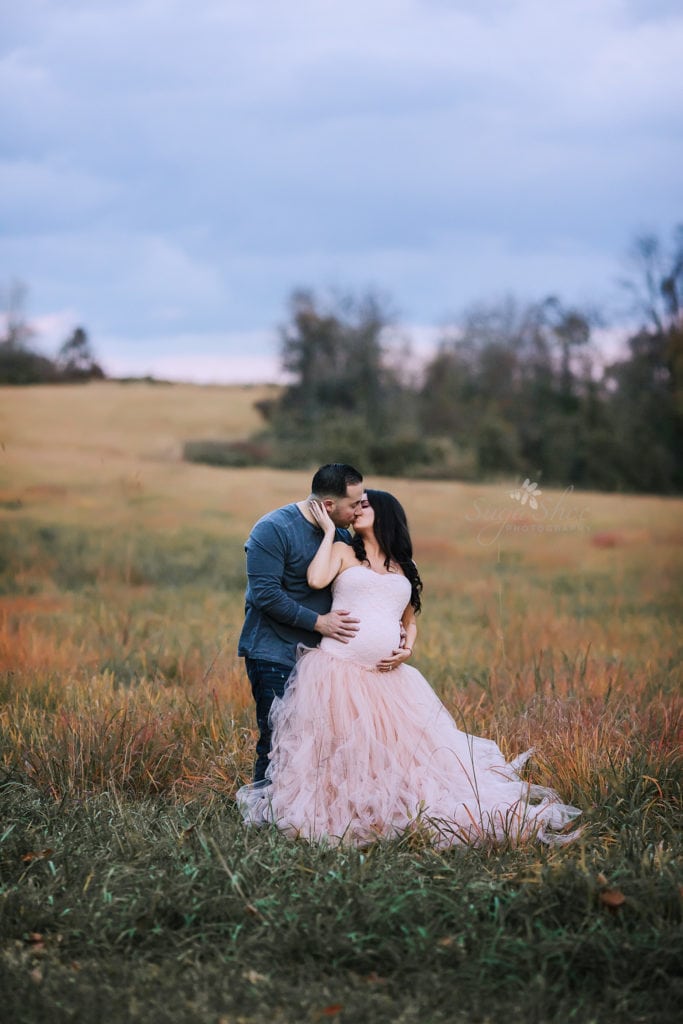 SugaShoc Photography Maternity Photographer Bucks County PA Doylestown PA Tyler State Park Maternity Session couple standing in field kissing woman wearing pink tulle maternity dress