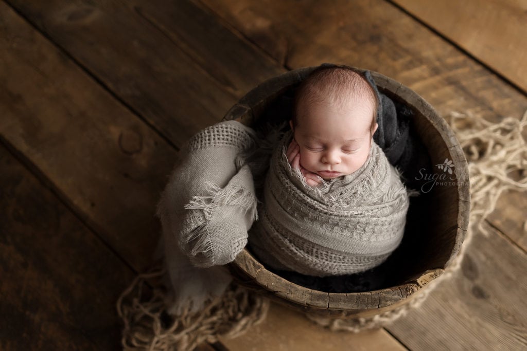 SugaShoc Photography Newborn Photographer Bucks County PA Doylestown PA Beckham Newborn Session baby sleeping wrapped in gray in wooden bucket on wooden floor