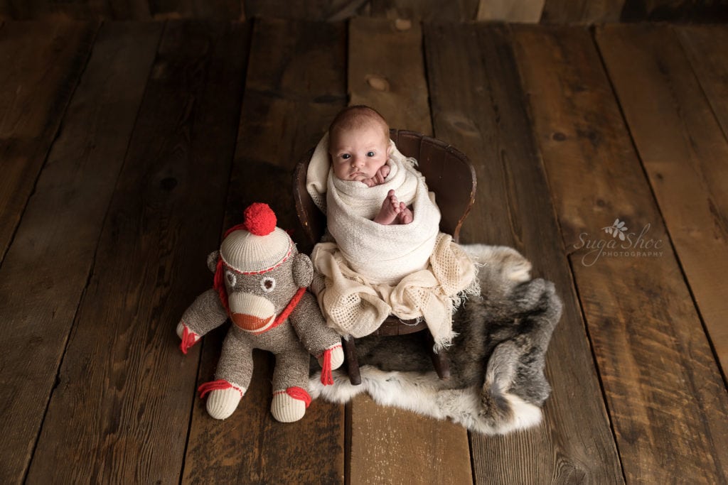 SugaShoc Photography Newborn Photographer Bucks County PA Doylestown PA Baby Hunter Newborn Session sitting in little wooden rocking chair on a fur trow wrapped in cream with stuffed monkey