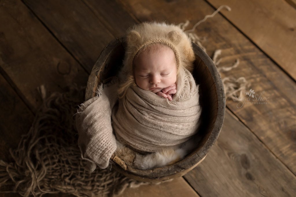SugaShoc Photography Newborn Photographer Bucks County PA Doylestown PA Baby Hunter Newborn Session sleeping wooden bucket wrapped in tan wrap wearing furry knit hat with ears
