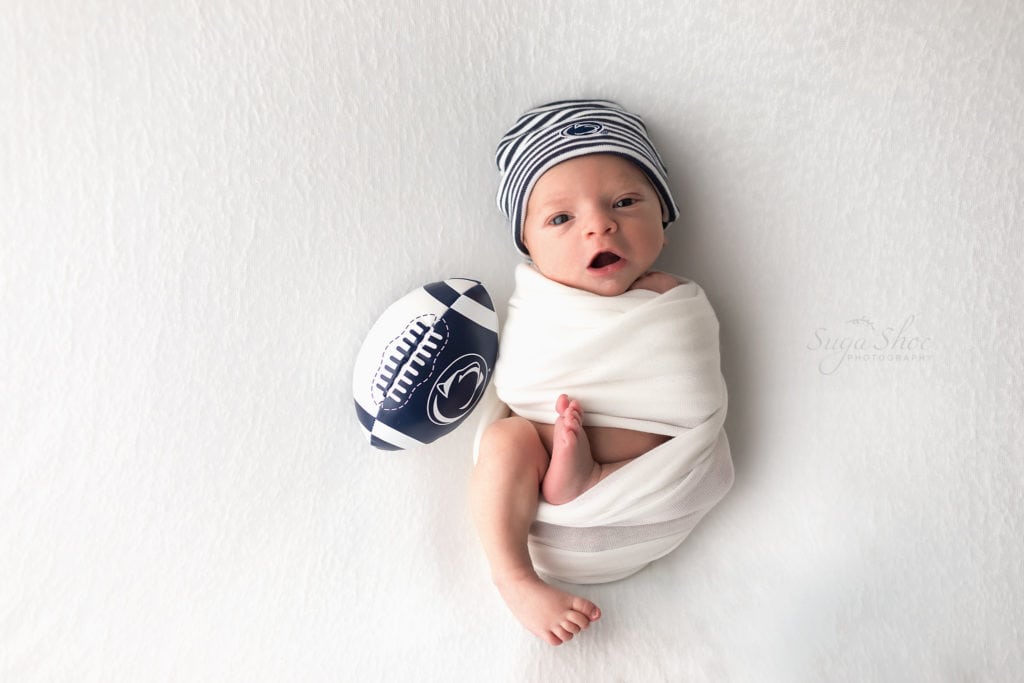 SugaShoc Photography Newborn Photographer Bucks County PA Doylestown PA Baby Hunter Newborn Session wrapped in white wearing Penn State hat and football awake