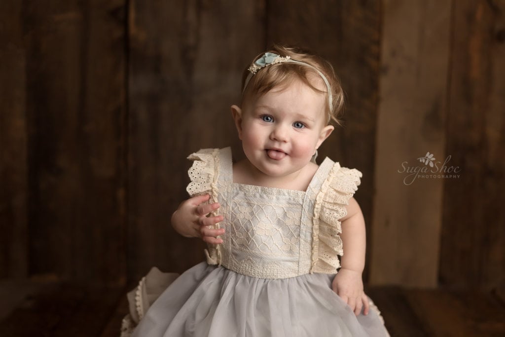 SugaShoc Photography Baby Photographer Bucks County PA Doylestown PA Cake Smash Session with Flowers baby dressing in pale blue and lace dress with her tongue sticking out