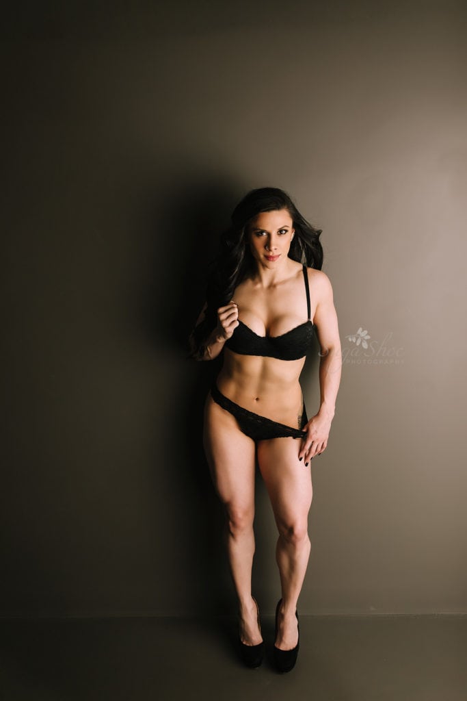 SugaShoc Photography Doylestown Boudoir Photographer PA Fitness Boudoir Session boudoir pose wearing black bra and panty holding bra cup and pulling down side on panty smiling