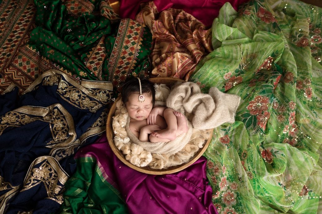 SugaShoc Photography Newborn photography newborn pose baby girl sleeping in wooden bowl surrounded by family saris