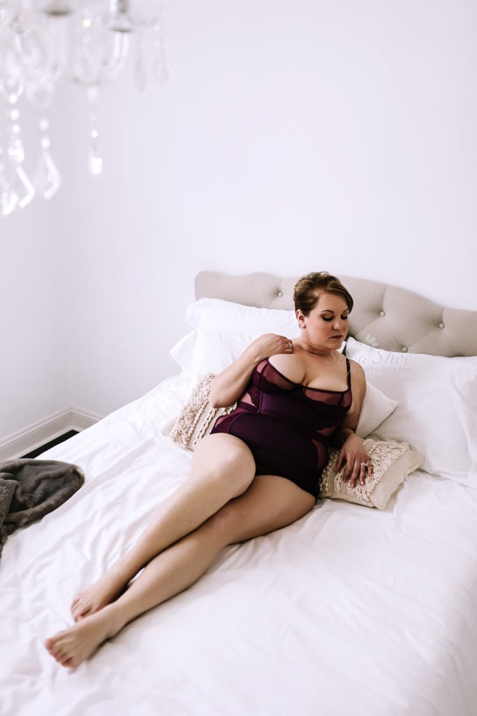 SugaShoc Photography Doylestown Boudoir Photographer PA Floral Boudoir Session boudoir pose laying on bed propped up on elbows wearing dark red teddy