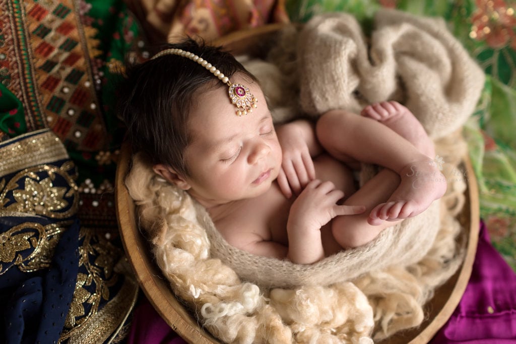 SugaShoc Photography Newborn Photography Bucks County PA Doylestown PA Newborn Photographer Sari Newborn Session baby sleeping in wooden bowl surrounded by Indian saris close-up