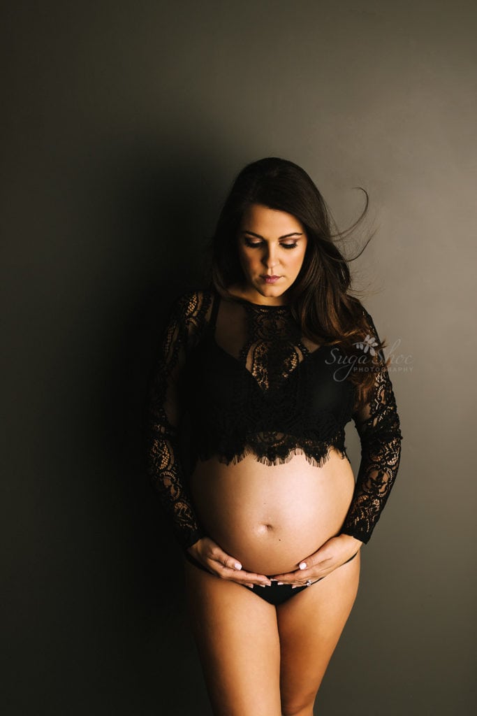 SugaShoc Photography Twin Maternity Session Bucks County PA Doylestown PA Maternity Photographer Maternity pose standing against dark wall wearing black lace top holding belly looking down