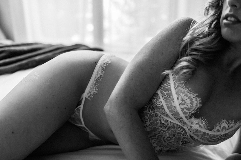 Sugashoc Photography Fiance Boudoir cloe up shot of laying on bed in white lace bra and panty in black-and-white