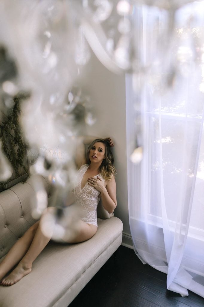 Sugashoc Photography Fiance Boudoir sitting on chaise in white teddy shot through chandelier