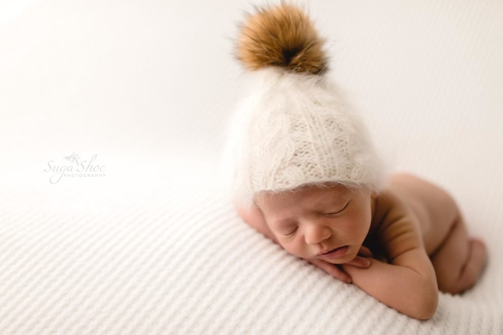 Fur Baby Newborn Session SugashocPhotography baby boy sleeping on white blanket with white knit hat with pom pom