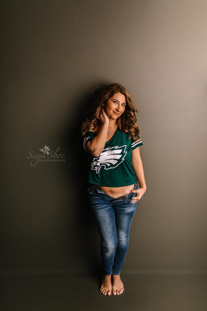 Love Reconnected Bucks County Boudoir Photographer - woman in jeans and eagles t-shit with neutral background behind