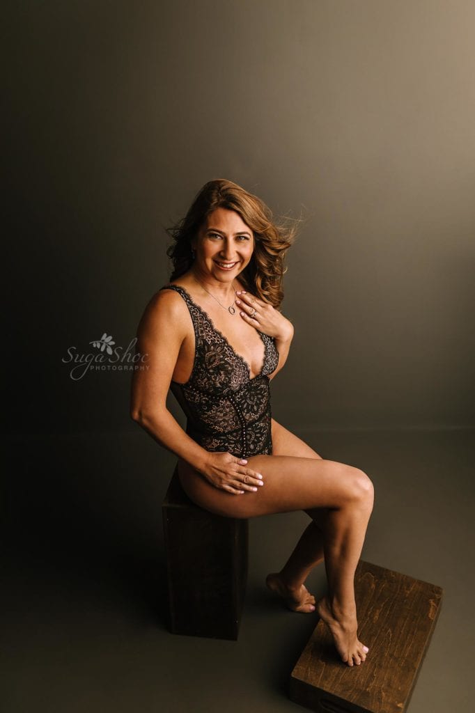 Love Reconnected Bucks County Boudoir Photographer - woman in boudoir pose, sitting on stool in front of neutral background in black 1 piece lingerie