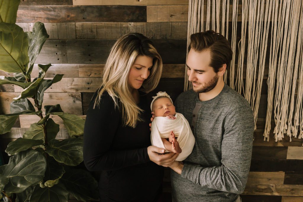 pa newborn photographer, mom and dad holding new baby girl against wood backdrop