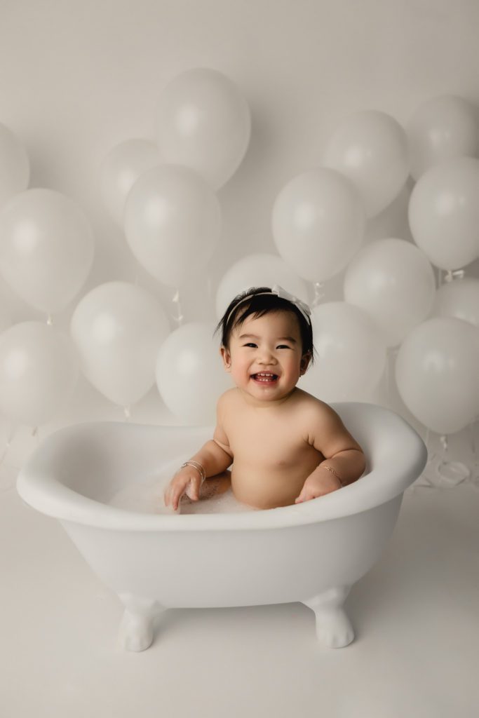 cake smash photo session, baby smiling in bubble bath with white balloons
