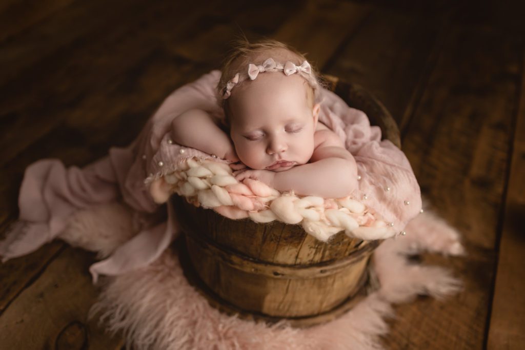 newborn in a wooden antique bucket with pink throw