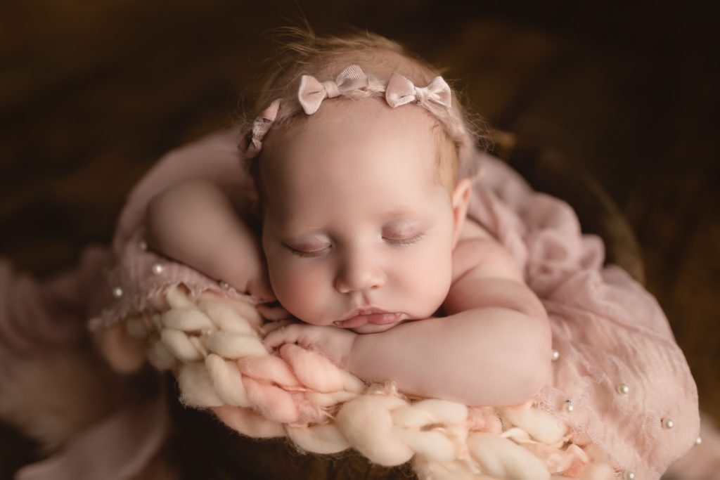 closeup of baby girl sleeping in wooden bucket wearing pink headband