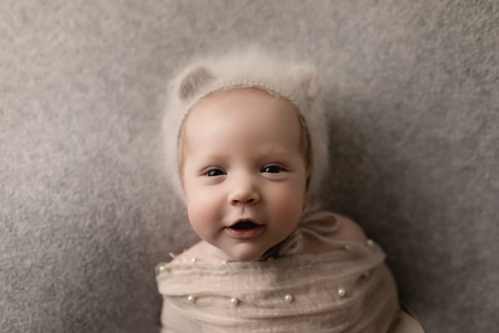 smiley baby girl wrapped in swaddle with bear cap