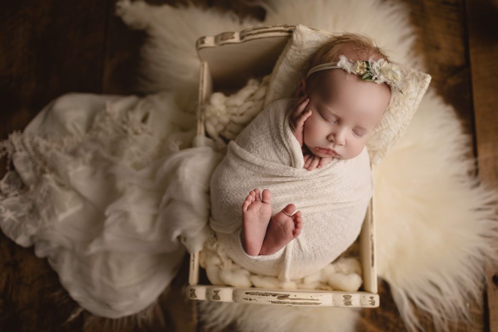 baby girl in white swaddle lying in wooden bed