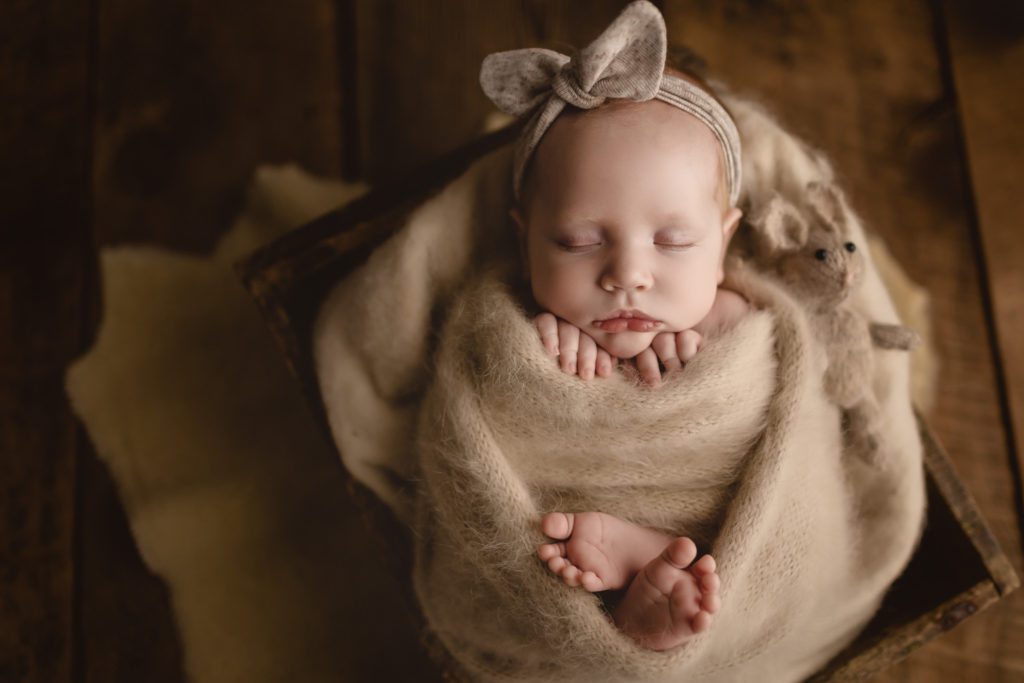 swaddled baby girl with headband in wooden box against rustic background