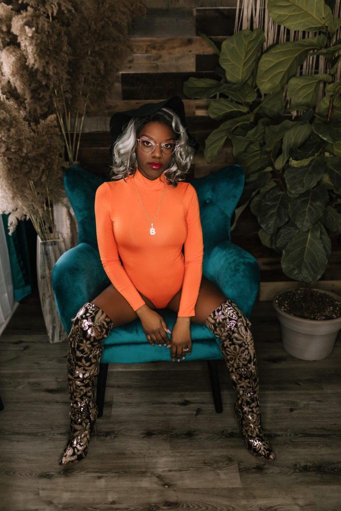 beauty photographer, woman wearing orange bodysuit and sitting on teal velvet chair