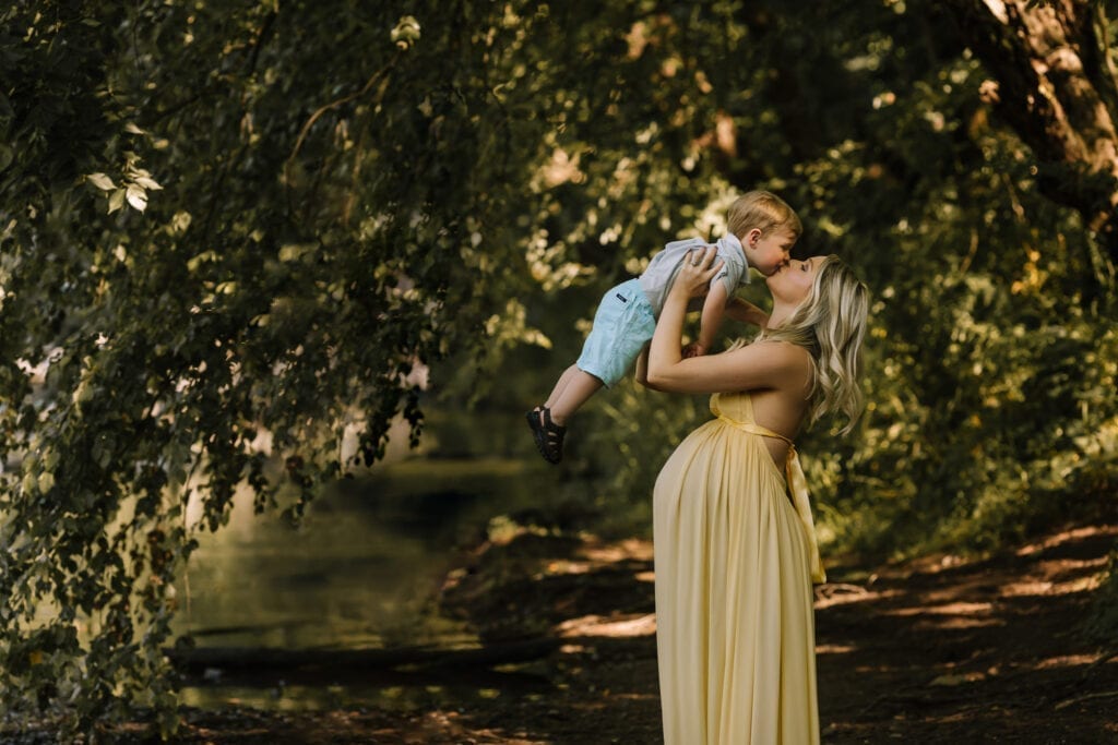 outdoor maternity session pa, mother in maternity gown holding son up for kiss