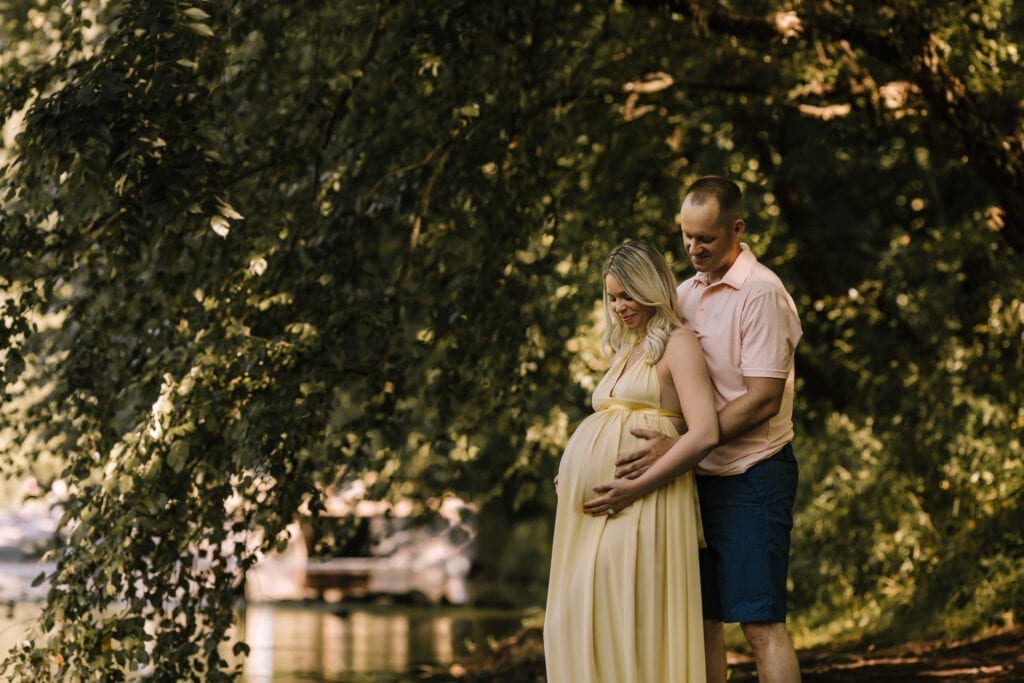 woman in maternity gown and husband standing near water