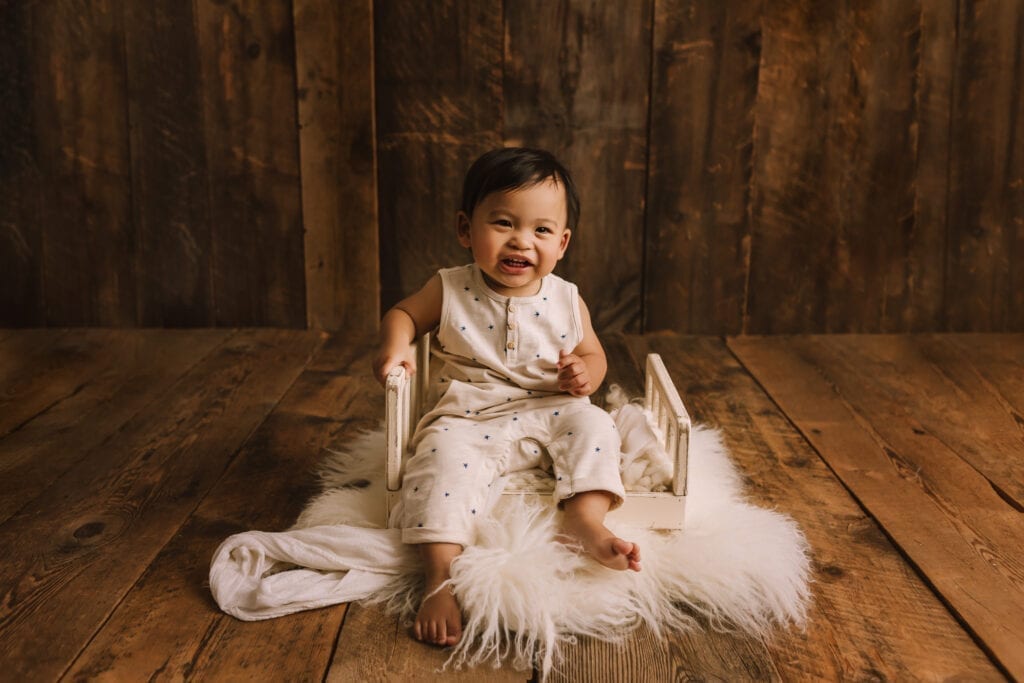 baby pictures, little boy in pjs sitting on bed with wood backdrop