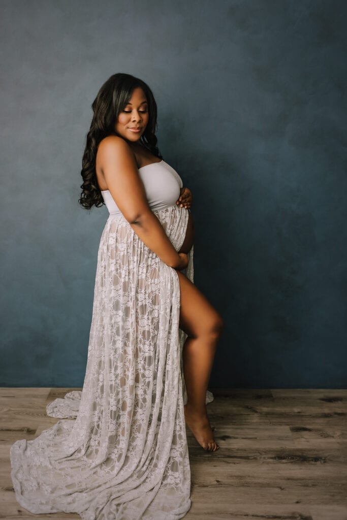 studio maternity portraits, woman wearing white maternity gown against gray backdrop
