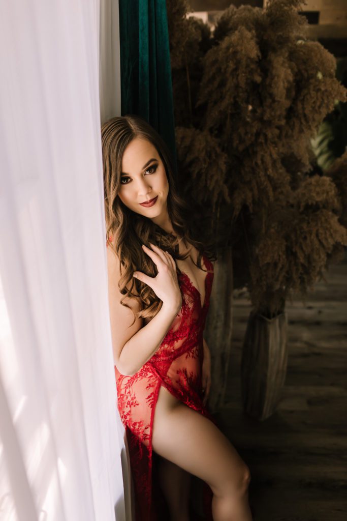 Woman in red lace underclothing leaning against curtained window