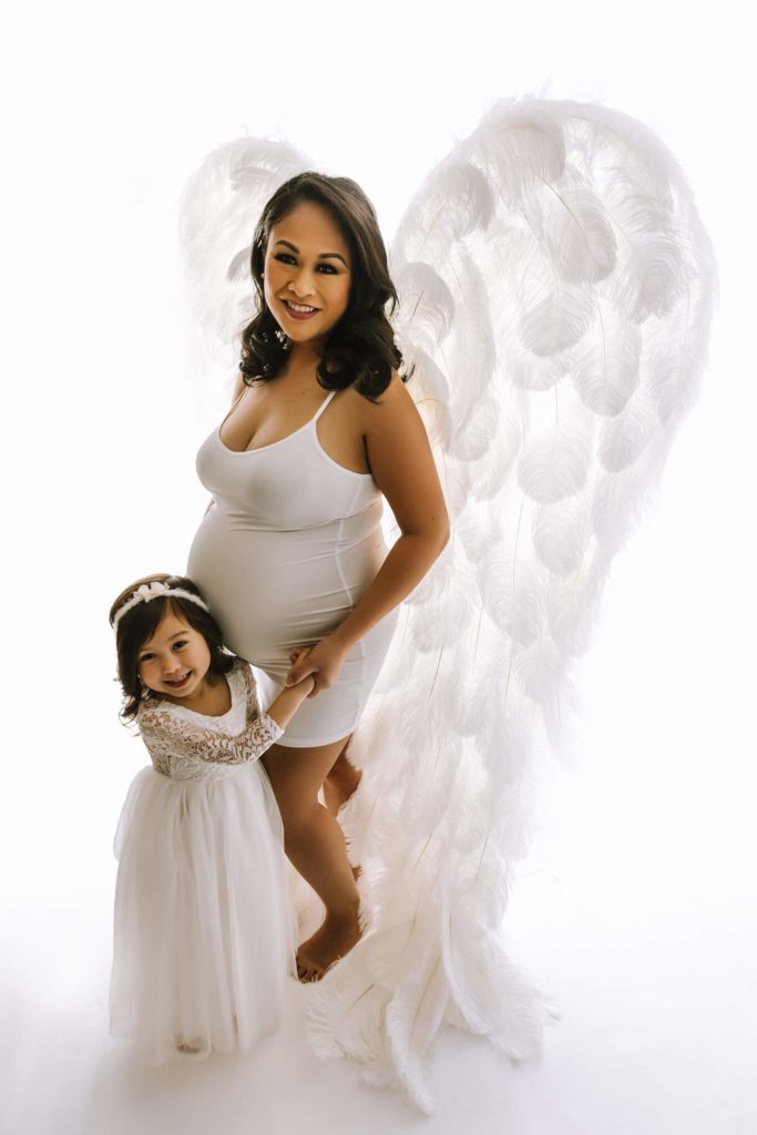 Mother with angel wings and daughter in studio maternity shoot.