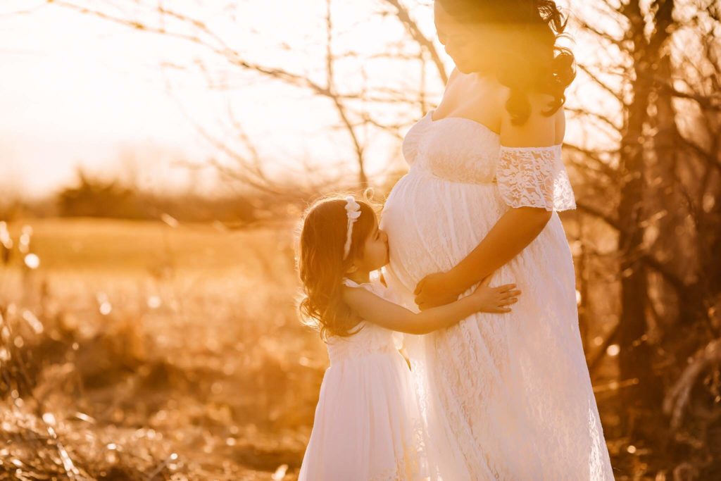 Mother and daughter family maternity shoot outdoors at sunset.