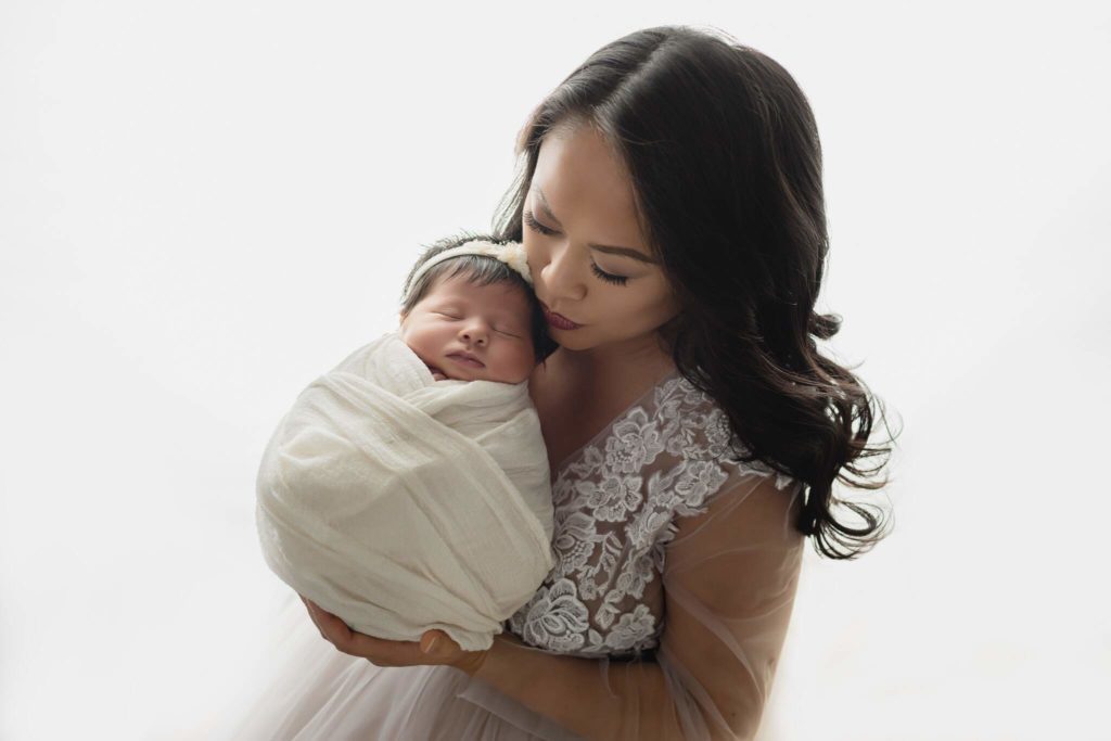 In studio mother and newborn photo shoot with white outfits and backdrop.