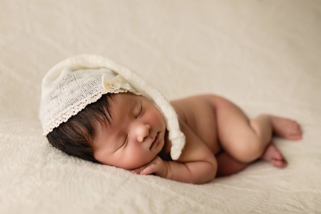Newborn baby girl sleeping photo shoot on white backdrop.