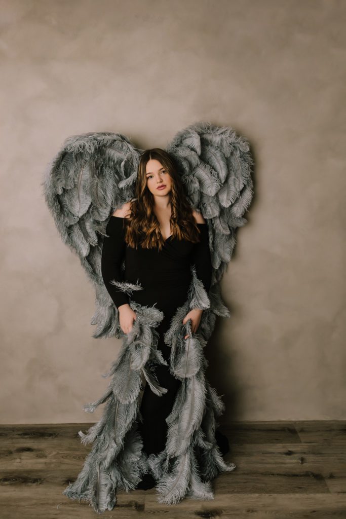 senior image with black dress and dark gray wings on beige backdrop